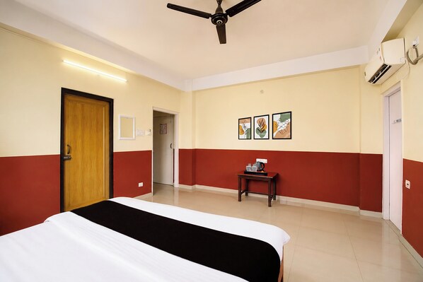 A hotel room with a bed, a table with a coffee maker, and a ceiling fan. - Hotel O City Centre Mall Formerly Stay (Guwahati)