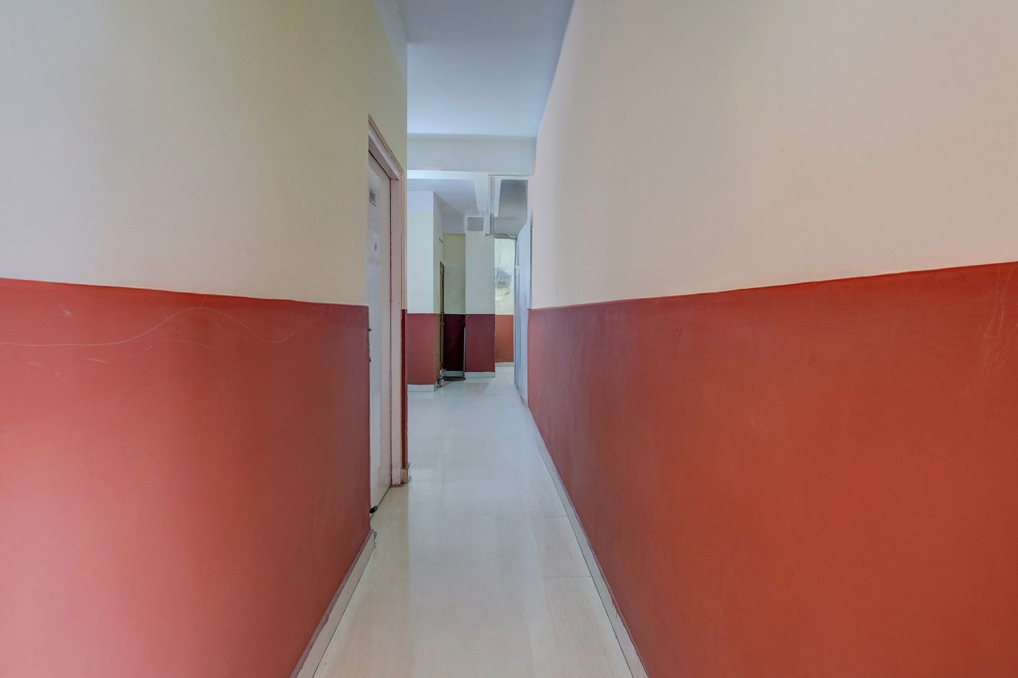 A corridor with red and white walls, leading to a door at the end.