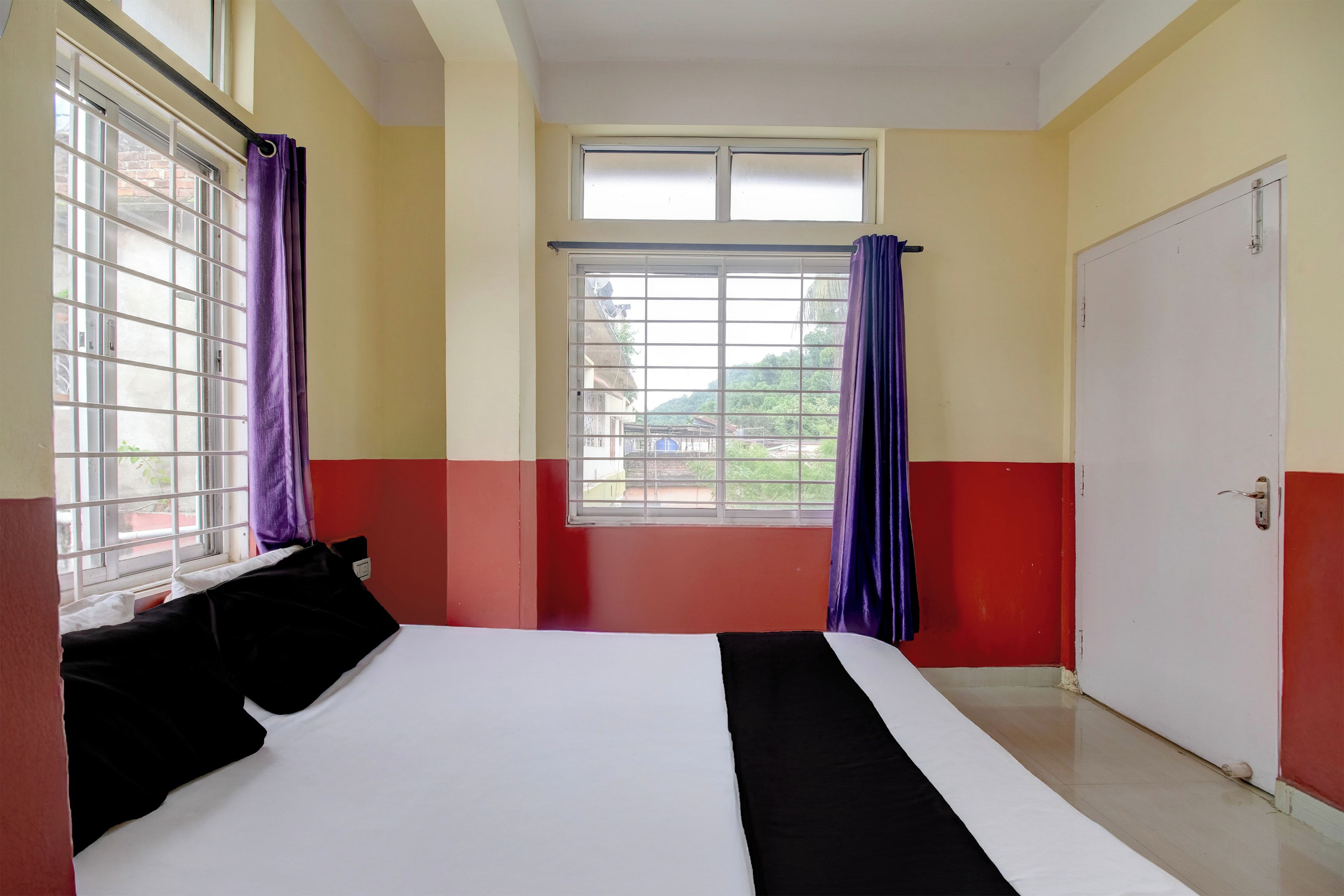 A hotel room with a bed, a window with curtains, and a door.