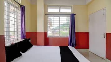 A hotel room with a bed, a window with curtains, and a door.