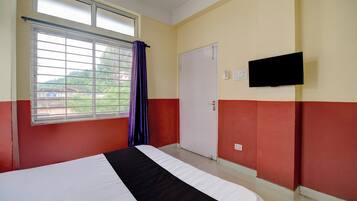 Habitación de hotel con cama, ventana con cortinas, puerta y televisor de pantalla plana montado en la pared.