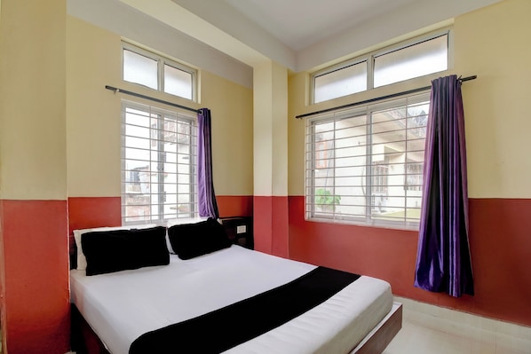 A hotel room with a bed, two windows with curtains, and a view of the outside.