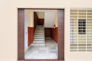 A corridor with a staircase leading to a landing, a fire extinguisher mounted on the wall, and a window with a metal grille.