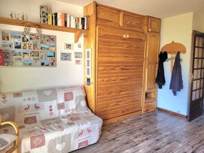 Ein gemütliches Zimmer mit einem Holzschrank, einer Couch mit gemustertem Bezug und einer Wand, die mit Fotos und Büchern geschmückt ist.