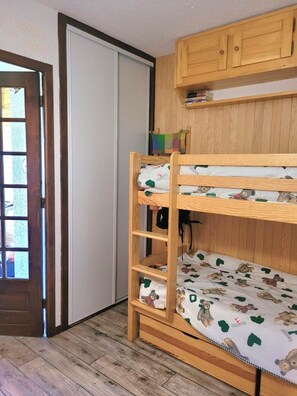 A bunk bed with a wooden frame and a mattress featuring a bear pattern. There is a wooden cabinet above the bed and a door with a window to the left. - Mountain Apartment for 4 People (Albiez-Montrond)