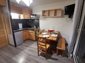 A compact kitchen with wooden cabinets, a microwave, a sink, and a dining table set with plates and cutlery. - Cozy Studio in Morillon (Morillon)