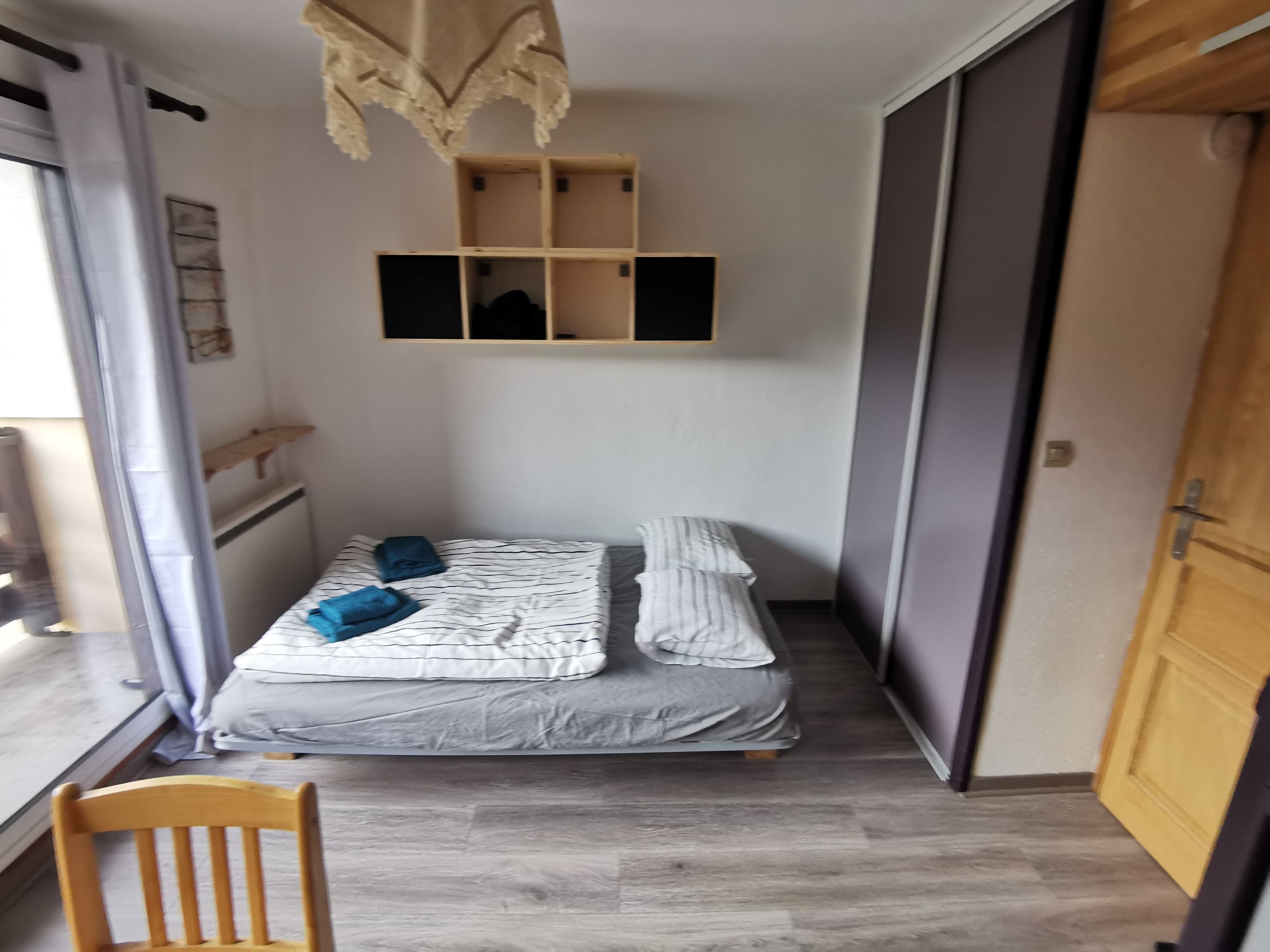A small, compact room with a bed, a chair, and a wardrobe.