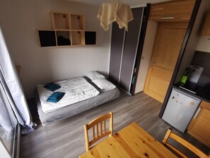 A compact room with a bed, a small table, a chair, a kitchenette, and a wardrobe. - Cozy Studio in Morillon (Morillon)