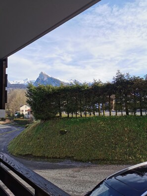 Uitzicht vanuit een raam op een parkeerplaats, een grashelling en een bergketen.
