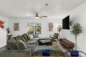 Ein Wohnzimmer mit Ecksofa, Couchtisch, Wand-Fernseher und Deckenventilator.