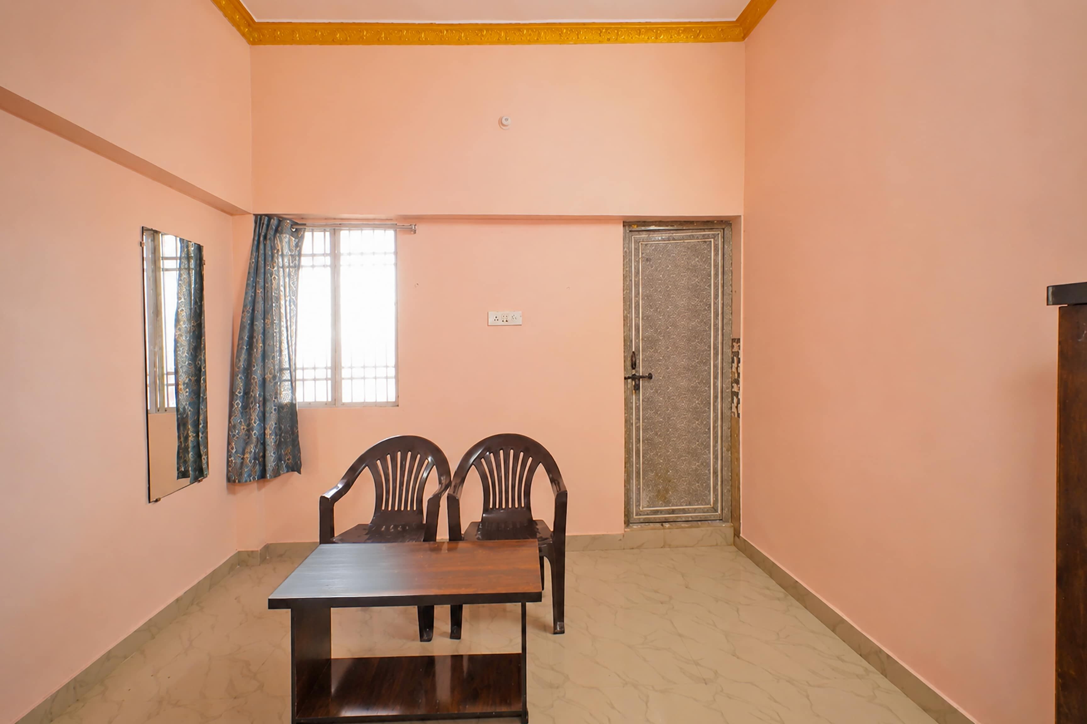 Une pièce avec une seule table et deux chaises, une fenêtre avec des rideaux, une porte et un interrupteur sur le mur.