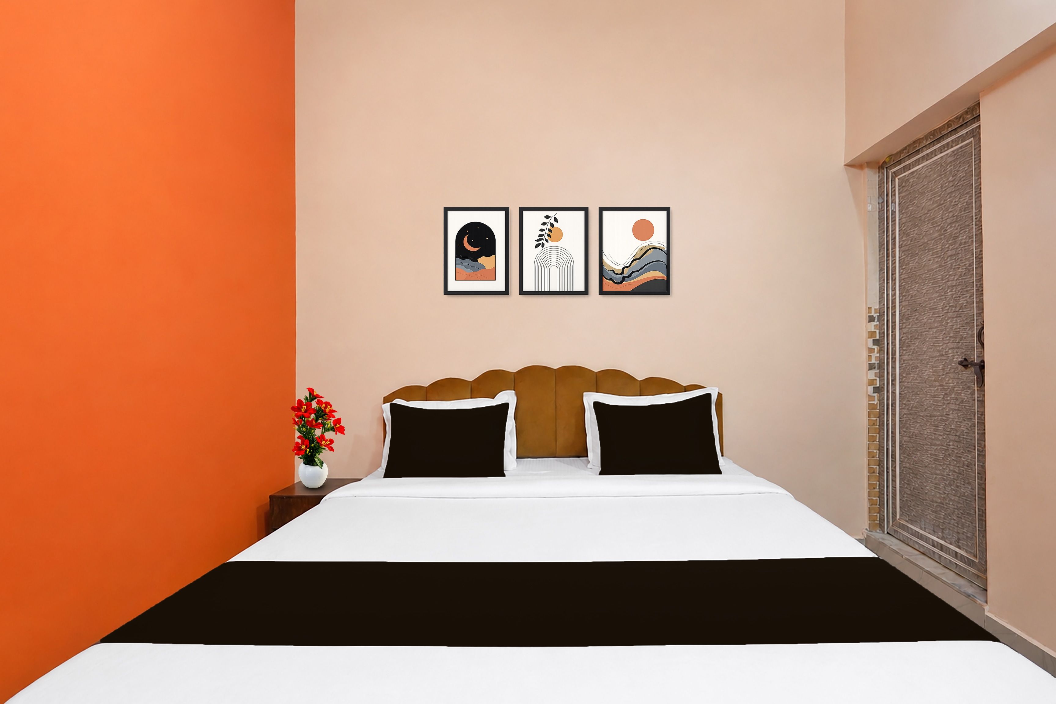 A bedroom with a bed, two pillows, a nightstand with a vase of flowers, and three framed artworks on the wall.