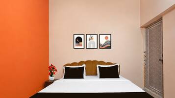 A bedroom with a bed, two pillows, a nightstand with a vase of flowers, and three framed artworks on the wall.