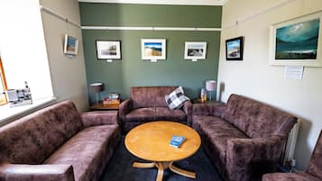 A room with a round wooden table, four cushioned chairs, a small side table with a lamp, and framed pictures on the wall.
