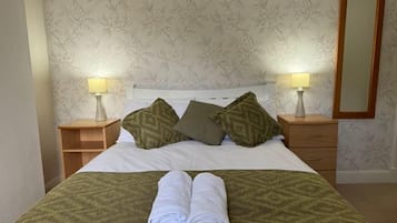 Een net opgemaakt bed met kussens, een gevouwen handdoek en twee bedlampjes.