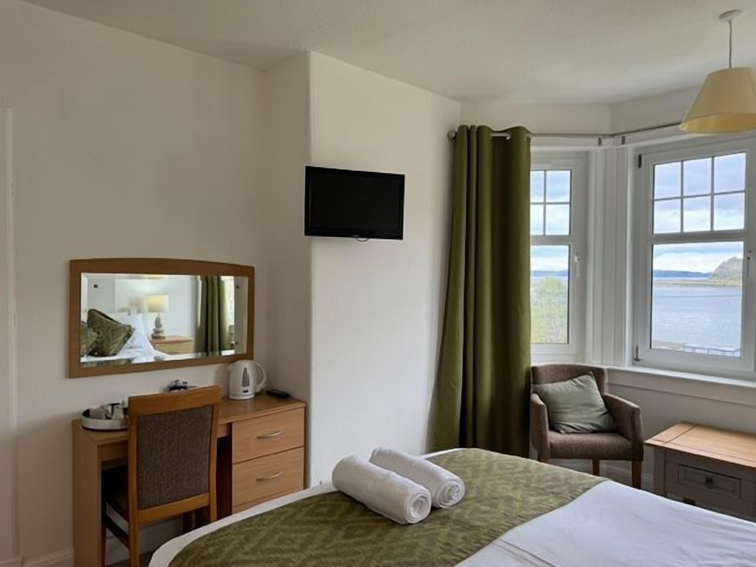 A hotel room with a bed, a desk, a chair, a television, and a window with curtains.