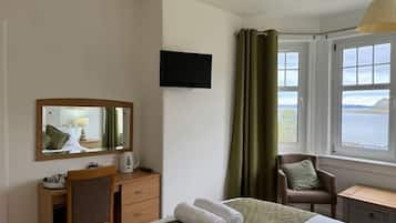 A hotel room with a bed, a desk, a chair, a television, and a window with curtains.