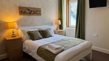 A bedroom with a bed, bedside tables, a flat-screen TV, and a window with curtains.