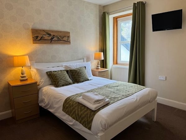 A bedroom with a bed, bedside tables, a flat-screen TV, and a window with curtains. - Lochranza Country Inn (Isle of Arran)