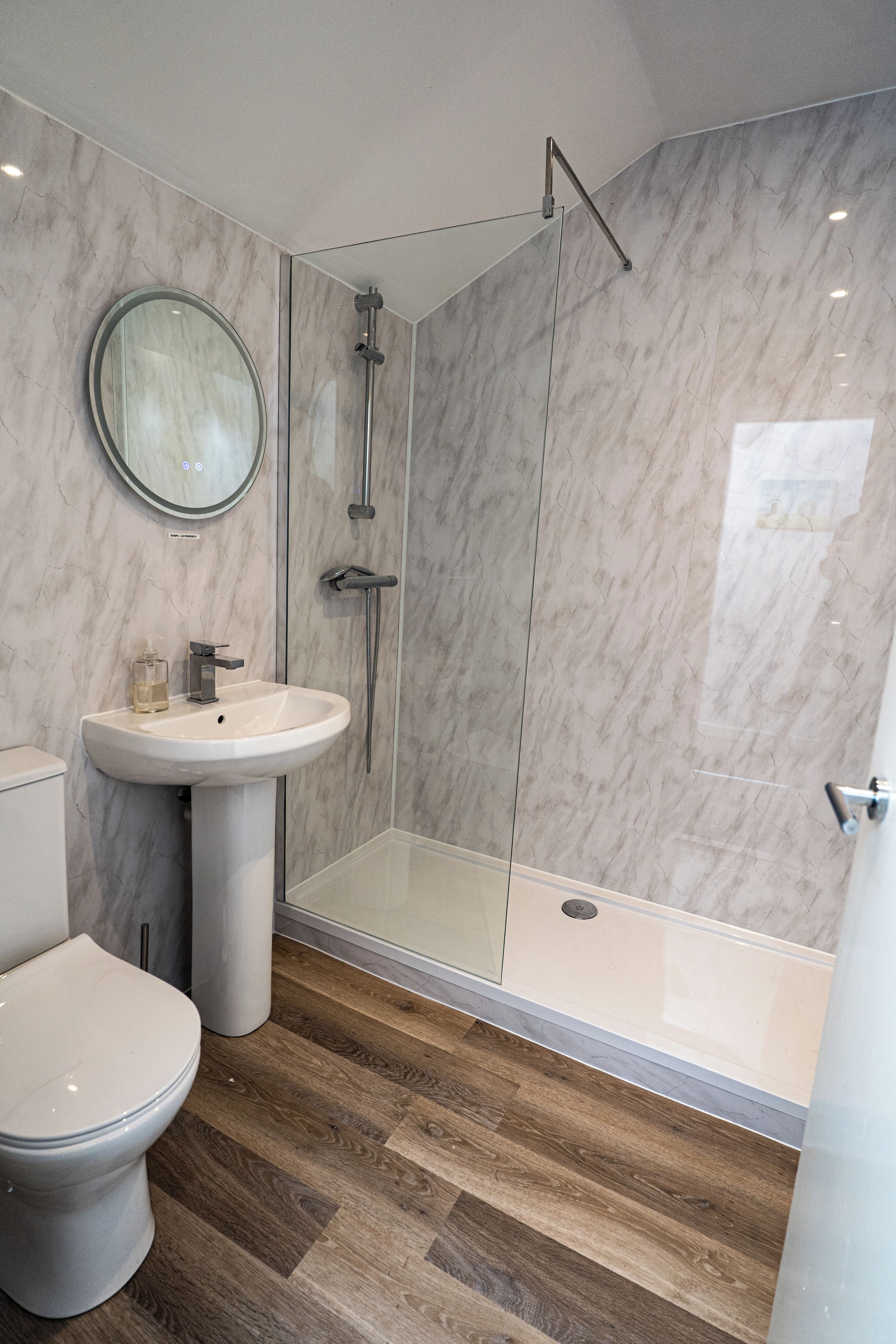 A modern bathroom with a glass-enclosed shower, a pedestal sink, and a toilet.