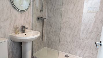 A modern bathroom with a glass-enclosed shower, a pedestal sink, and a toilet.