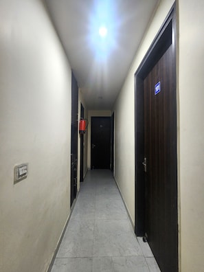 A hallway with a ceiling light, a door with a blue sign, and a wall-mounted electrical outlet. - Oly Hotel Star Inn (New Delhi)