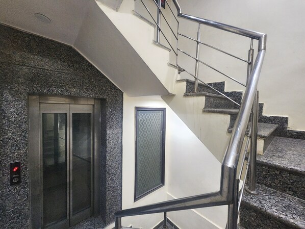 A staircase with metal railings and granite steps, leading to an elevator. - Oly Hotel Star Inn (New Delhi)