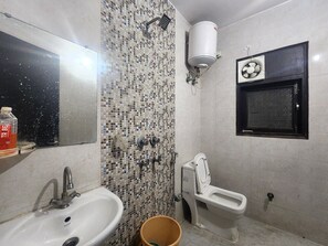 A bathroom with a sink, a toilet, a shower, and a wall-mounted heater. - Oly Hotel Star Inn (New Delhi)