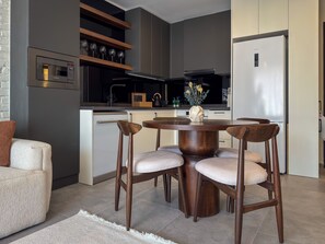 Eine moderne Küche mit Einbauofen, einem Essbereich mit rundem Tisch und vier Stühlen sowie einem Kühlschrank.