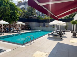 A swimming pool with lounge chairs and umbrellas, surrounded by a tiled deck and a geometric patterned wall. - Qoople Prive 42 - Cozy 1-bedroom apartment in Alanya (Alanya)