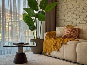 A living room with a sofa, a potted plant, a glass coffee table, and a brick wall. - Qoople Prive 42 - Cozy 1-bedroom apartment in Alanya (Alanya)