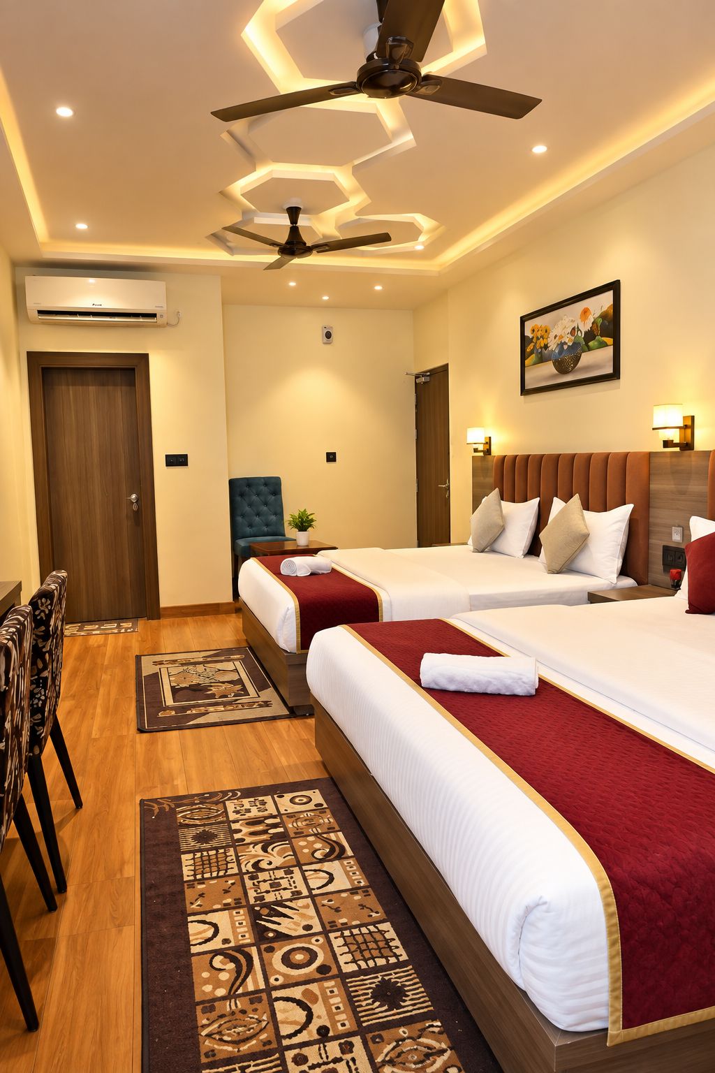 Une chambre d’hôtel avec deux lits, un ventilateur de plafond, un appareil de climatisation, un tableau au mur et un tapis à motifs.