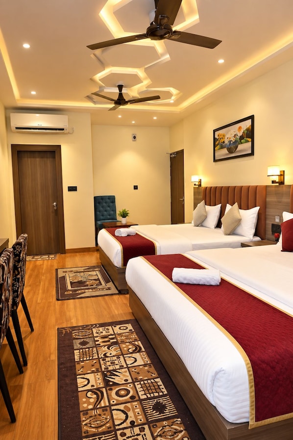 A hotel room with two beds, a ceiling fan, an air conditioning unit, a painting on the wall, and a patterned rug. - Hotel Arcadia Awadh Ayodhya (Ayodhya)