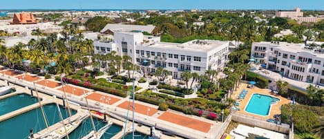 A marina with multiple boats docked, a swimming pool, and buildings with balconies overlooking the water.