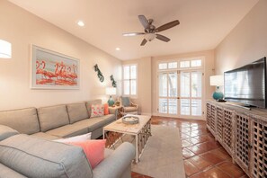 A living room with a sofa, a coffee table, a TV on a wooden cabinet, and a ceiling fan. - A SAFE HARBOUR : 2  BR, 2  BA Condominium in Key West, Sleeps 4 (Key West)
