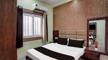 Una habitación de hotel con cama, mesita de noche, espejo, ventana con cortinas y aire acondicionado.