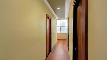 A narrow hallway with wooden flooring and doors on both sides, leading to a room with a window.