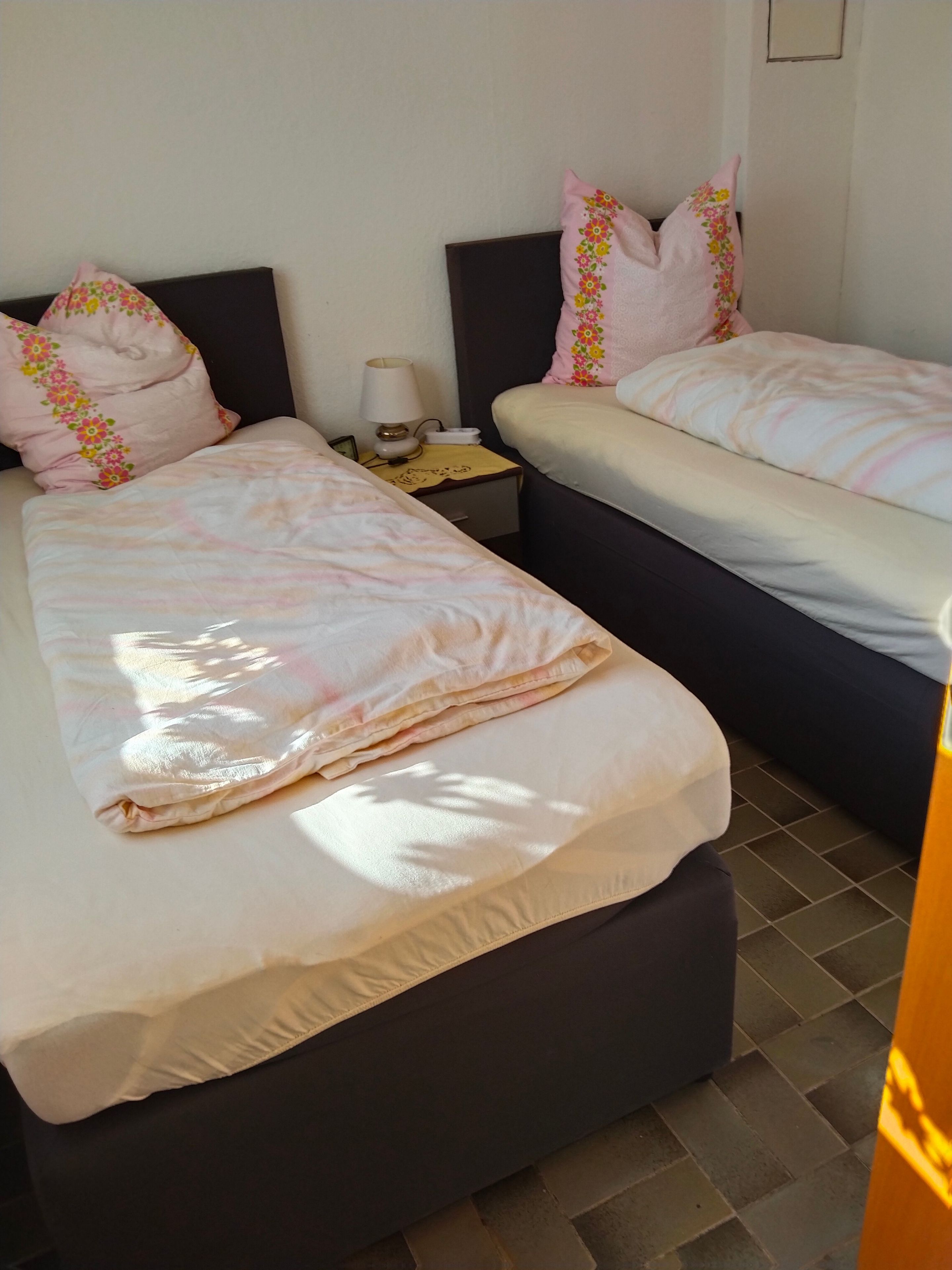 Ein Hotelzimmer mit zwei Betten, jedes mit einem Kissen und einem Nachttisch mit einer Lampe.