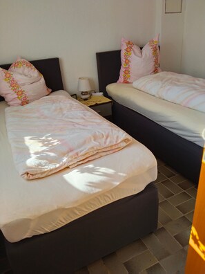 A hotel room with two beds, each with a pillow and a bedside table with a lamp.