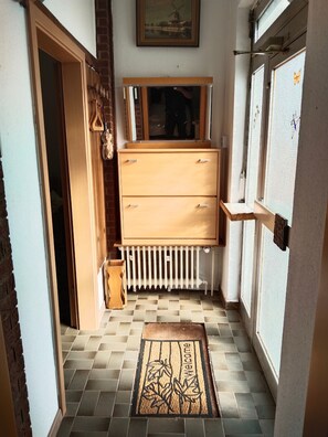 A narrow hallway with a wooden dresser, a radiator, and a welcome mat.