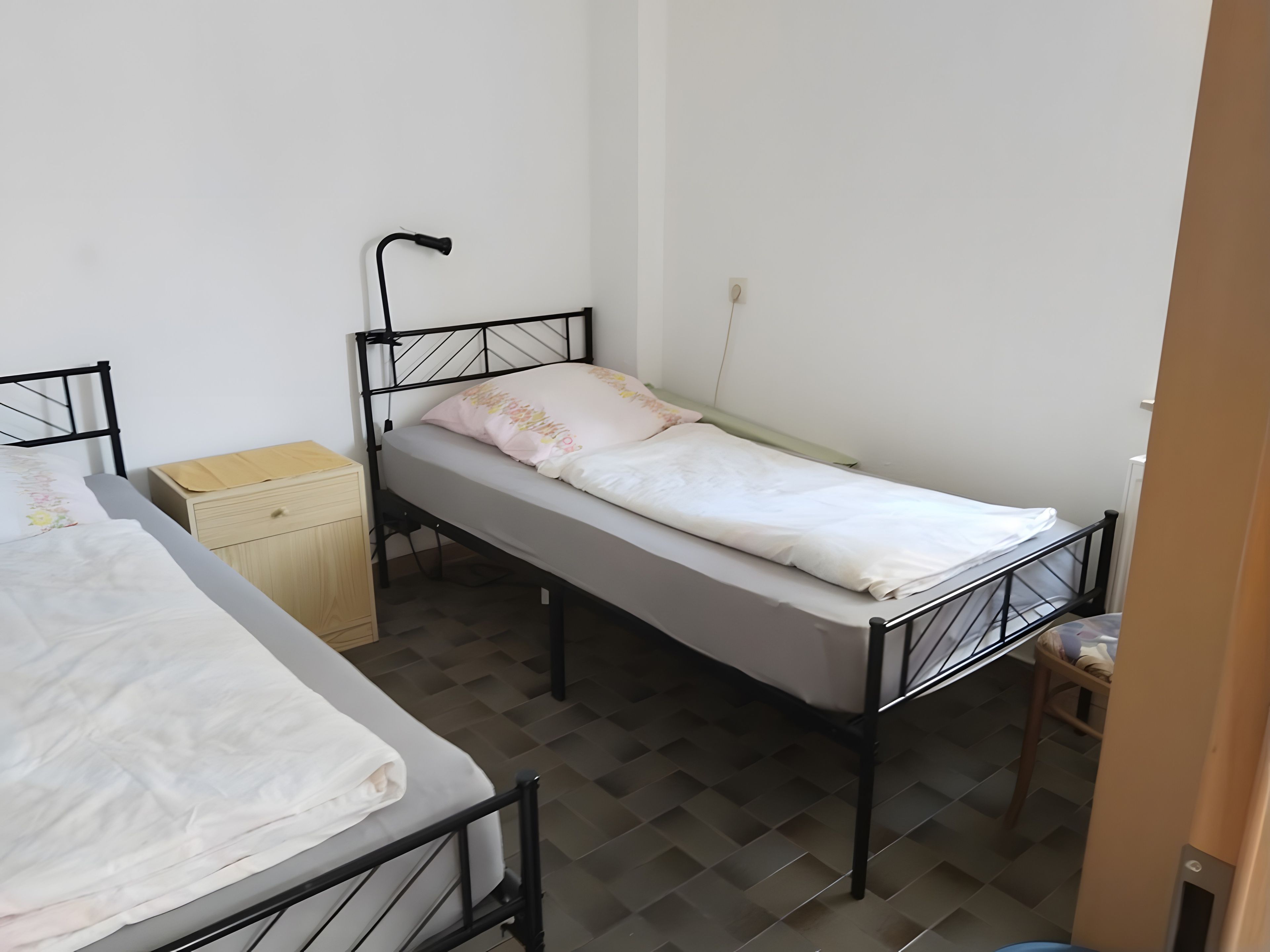 A single bed with a headboard, a bedside table, and a wall socket.