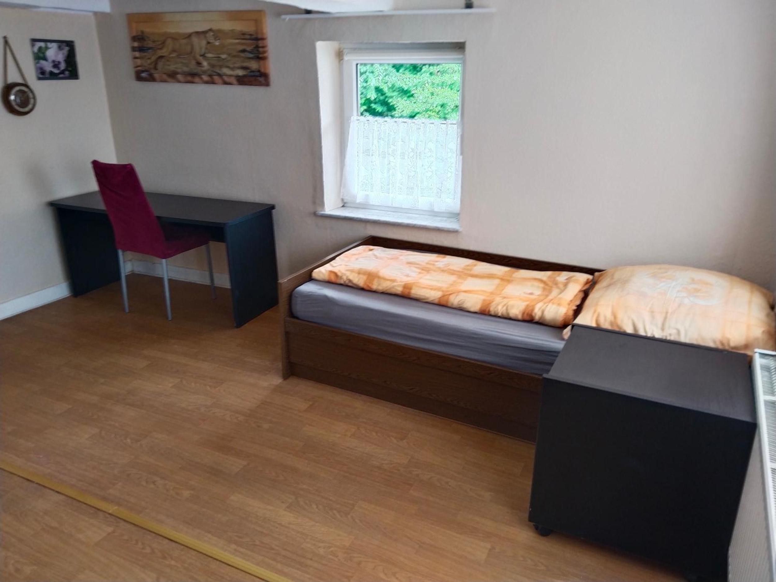 Ein Schlafzimmer mit Bett, Schreibtisch und Stuhl. Ein Fenster bietet Blick auf Grünflächen außerhalb.