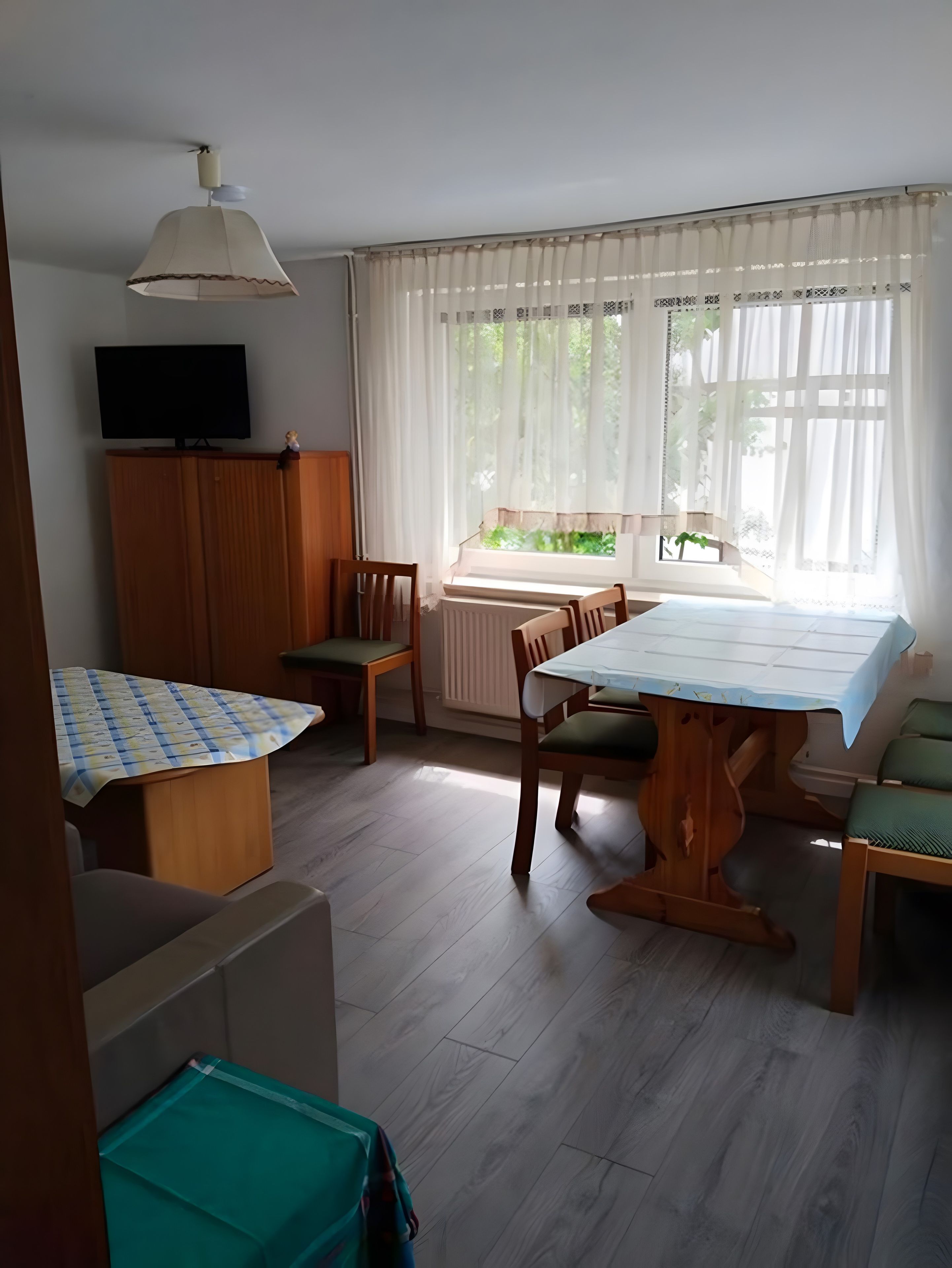 Ein Zimmer mit Esstisch, Stühlen, einem Fernseher auf einer Kommode und einem Fenster mit Vorhängen.
