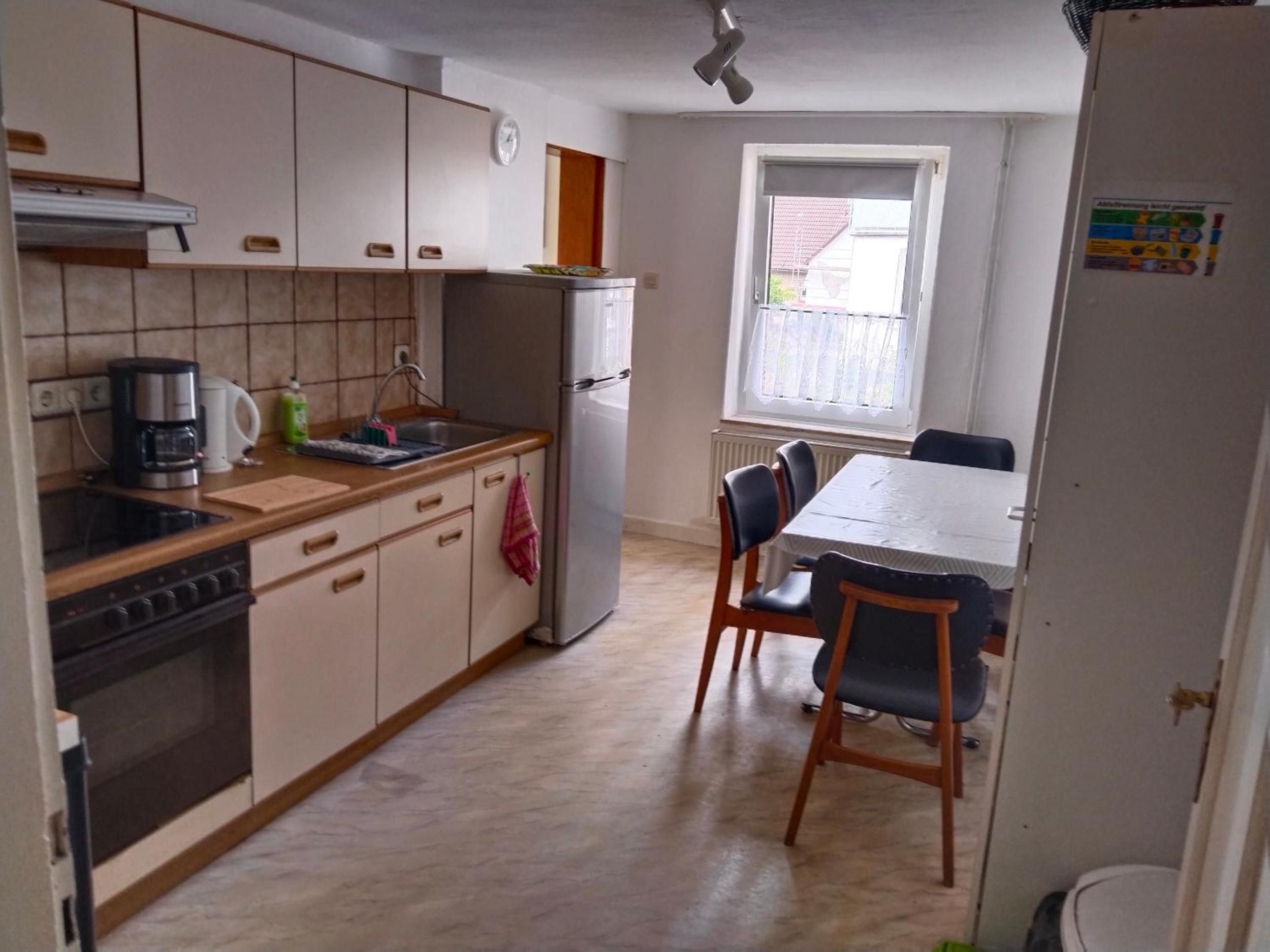 Cocina compacta con refrigerador, estufa y cafetera. Hay una mesa de comedor con sillas y una ventana con vistas.