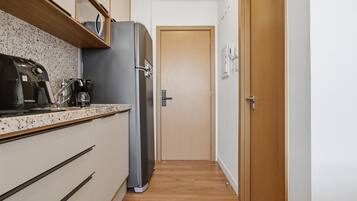 Een smalle keuken met een koelkast, koffiezetapparaat en een houten deur aan het einde.
