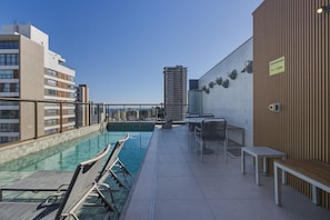 Ein Pool auf dem Dach mit Liegestühlen und Tischen, im Hintergrund ein Hochhaus und ein Schild, das eine Höhe von 1,22 m angibt.