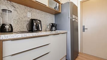A kitchen with a granite countertop, a coffee maker, a blender, and a stainless steel refrigerator.