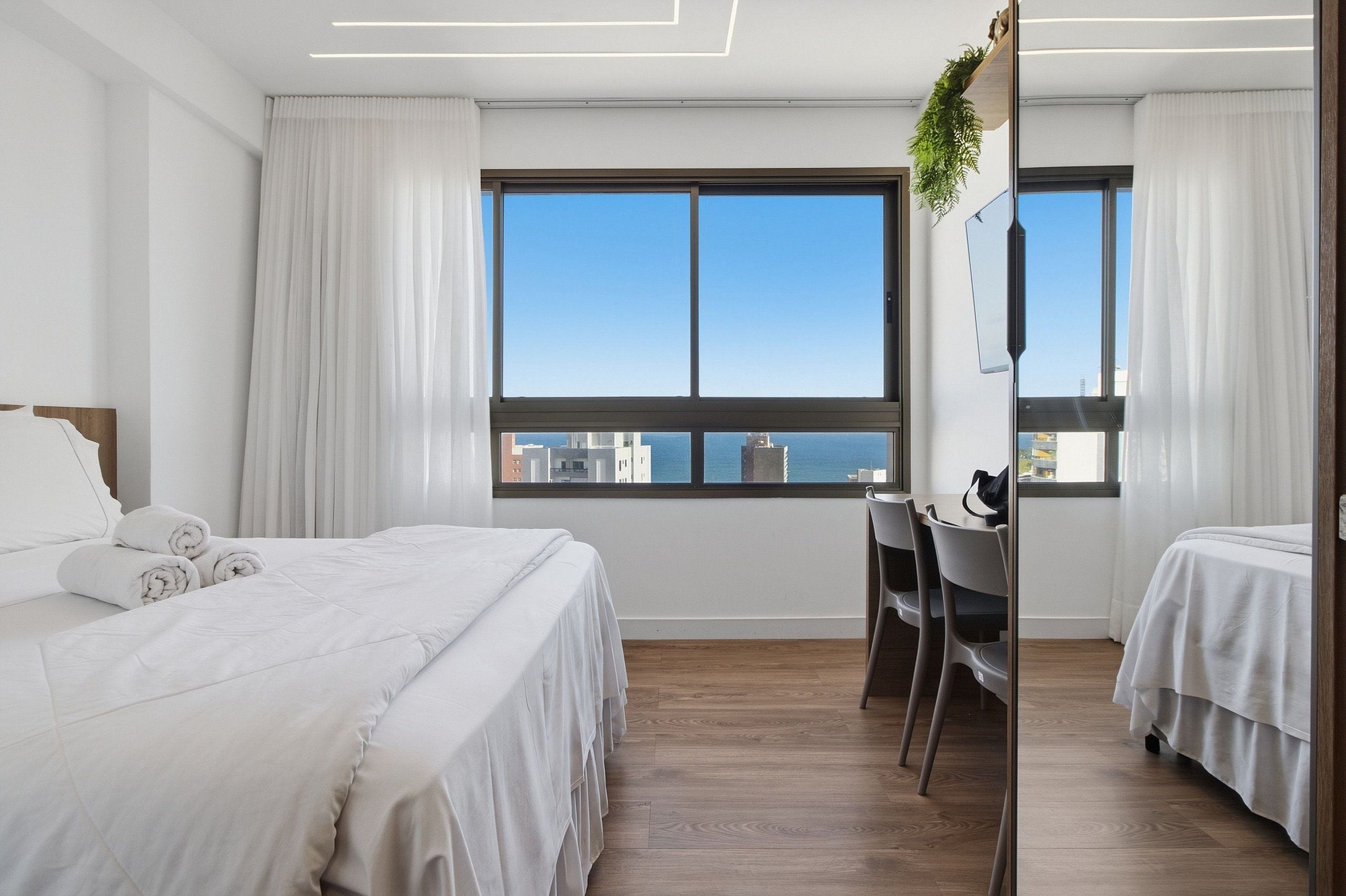 Een hotelkamer met een bed, een bureau en uitzicht op de stad door grote ramen.