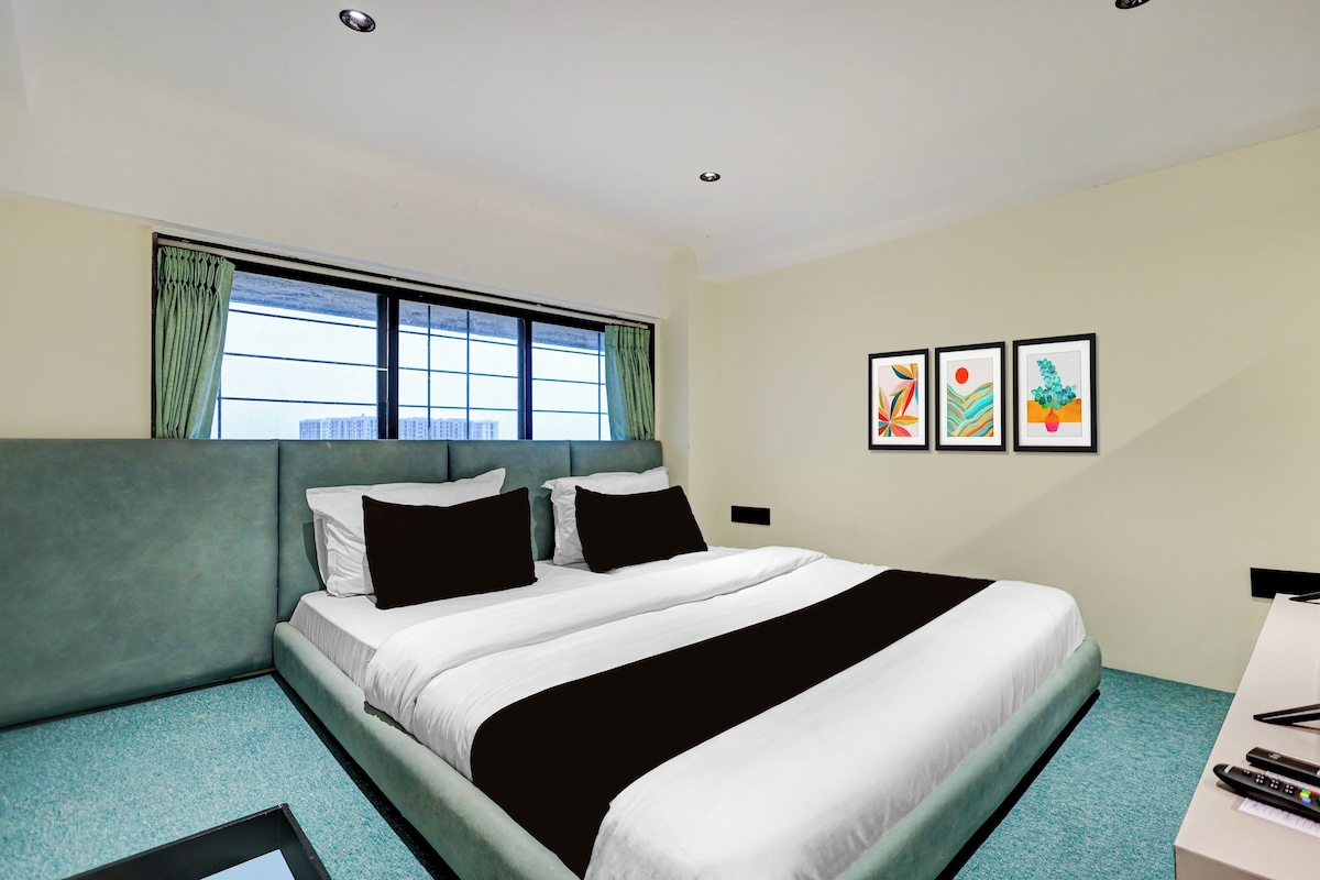 A hotel room with a bed, a window with curtains, and three framed artworks on the wall.