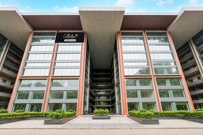 Un edificio moderno con una entrada amplia, varios pisos y un letrero que indica que se trata de un conjunto de apartamentos con servicios.